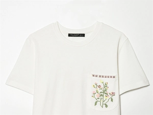 Detail der floralen Kreuzstich-Stickerei auf der Brusttasche eines weißen Baumwoll-T-Shirts