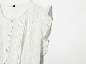 Detail of white sleeveless cotton blouse featuring ruffles and vertical hollow lace trim