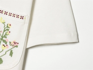 Detailansicht der Blumen-Kreuzstich-Stickerei und Tasche auf dem weißen Strickshirt