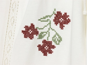 Detail der roten Kreuzstich-Blumenstickerei und weißer Spitze auf weißem Stoffgewebe