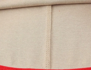 Macro shot of meticulous red trim stitching on beige knitted fabric showing quality craft