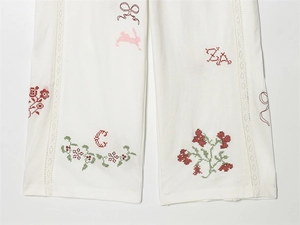 Nahaufnahme weißer Hosen mit Blumenstickerei und Spitzenbesatz am Saum der Beine