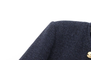 Détail macro du blazer en laine bleu marine avec tissu texturé et bouton doré brillant