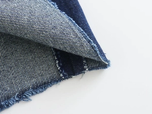 Primer plano del tejido vaquero azul oscuro con textura de sarga y bordes deshilachados
