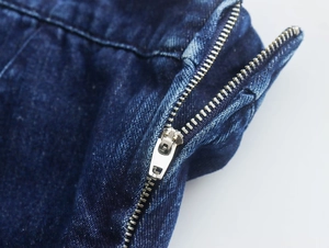 Primer plano de cremallera metálica en vestido de tela vaquera azul oscuro lavado