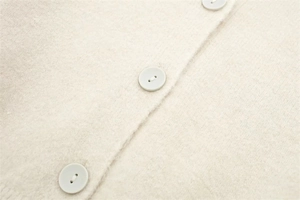 Detailed close-up of soft cream knit cardigan texture and matching buttons