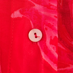 Macro detail of a pearl button on red floral sheer chiffon fabric with precise stitching