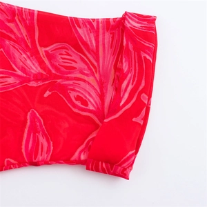 Detailed macro view of vibrant red chiffon fabric with pink tropical leaf print and neat edges