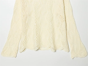 Detail of cream white knit sweater featuring delicate diamond hollow patterns and wavy hems
