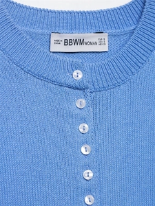 Detail of blue knit cardigan featuring pearl buttons and ribbed round neckline texture