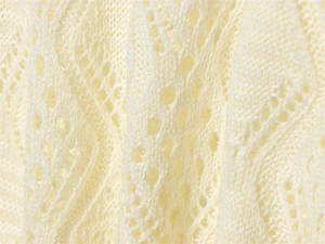 Close-up of cream hollow pointelle knit fabric with diamond pattern texture details