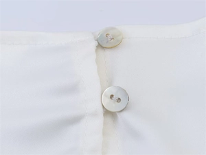 Detail der weißen Satinbluse mit glatter Stoffstruktur und Knöpfen in Perlglanz-Optik