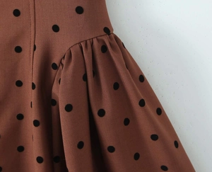 Detail van een karamelbruine jurk met stippen en elegante geplooide pofmouwen