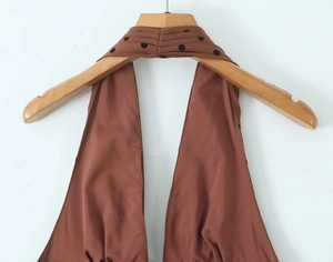 Detailweergave van donkerbruine halterjurk met geplooide zwart gestippelde nekband