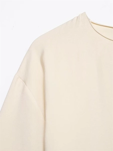 Detail of crew neck and dropped shoulders on this cream-colored pleated midi dress