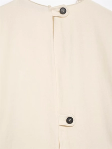 Close-up of pleated beige midi dress featuring dark buttons and precise tab closure details