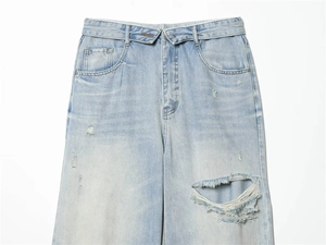 Close-up of light blue distressed denim jeans with frayed holes and vintage whiskers