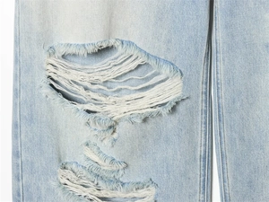 Close-up detail of heavy washed light blue denim jeans with distressed ripped texture