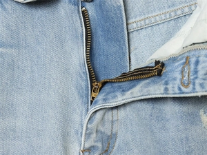 Close-up detail of high-quality metal zipper and twill texture on light blue denim jeans