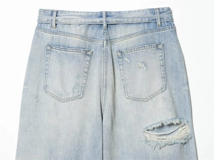 Detail view of light blue distressed denim back pockets and ripped fabric textures
