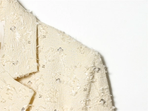 Detail eines cremefarbenen Blazers mit Reliefstruktur, Pailletten und Perlenstickerei
