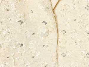 Detailansicht der cremefarbenen Tweedjacke mit Paillettenstickerei und Stoffknopf