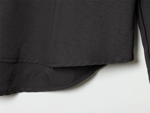 Close-up of a curved hem on a black woven shirt with precise stitching and clean seams