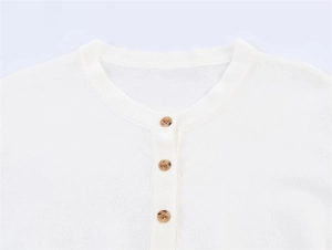 Detail der weißen Strickjacke mit bernsteinfarbenen Knöpfen und feiner Textur