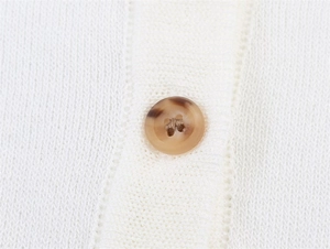 Detail aus weißem Feinstrick mit einem bernsteinfarbenen Knopf in Marmoroptik am Cardigan