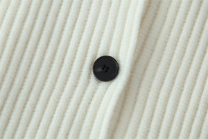 Close-up of white ribbed knit cardigan fabric featuring a contrasting black button