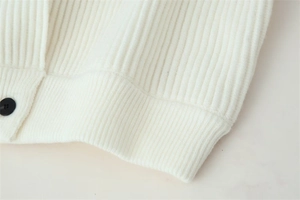 Detail of white knit cardigan showing vertical ribbed texture and black button accent