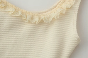 Detail shot of the ribbed knit fabric and delicate lace trim on the cream tank top
