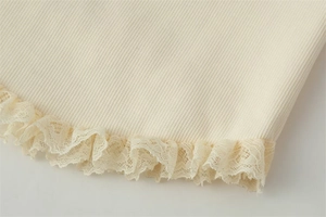 Detailed macro view of cream ribbed knit fabric featuring delicate lace trim edging