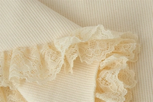 Close-up of cream ribbed knit fabric with delicate lace trim and ruffled edge detail