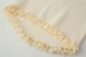 Detail of beige ribbed knit hem with delicate lace trim and ruffle edge texture