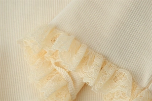 Macro detail of ribbed knit fabric texture with ruffled lace trim on a cream women top