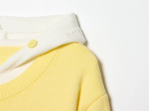 Dettaglio di cardigan in maglia gialla con colletto bianco a contrasto e bottone