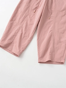 Détail du pantalon rose à jambes larges montrant le cordon à embouts dorés et le tissu texturé