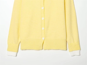 Dettaglio cardigan in maglia giallo tenue con bottoni bianchi e texture a coste