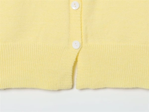 Dettaglio del cardigan in maglia giallo chiaro con bottoni bianchi e bordo a coste