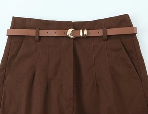 Dettaglio dei pantaloni a vita alta con cintura sottile in pelle marrone e fibbia oro
