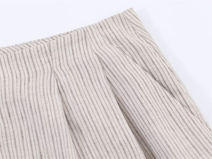 Detalle de la cintura plisada en pantalones de lino crema con finas rayas diplomáticas