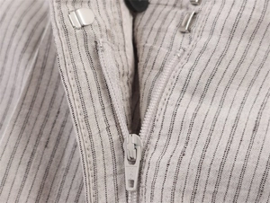 Detalle del pantalón de rayas beige claro que muestra la cremallera YKK y el cierre