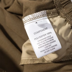 Etichetta di cura che mostra 100% poliestere e istruzioni di lavaggio su pantaloni marroni