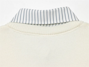 Détail d'un pull en maille crème superposé sur un col de chemise à rayures bleues