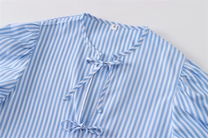 Dettaglio dello scollo della camicia a righe blu con fiocchi e etichetta della taglia