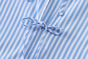 Dettaglio della camicia a righe bianche e blu con un fiocco sulla chiusura anteriore centrale