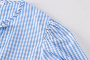 Dettaglio camicia in popeline a righe bianche e blu con fiocco al collo e pieghe spalla