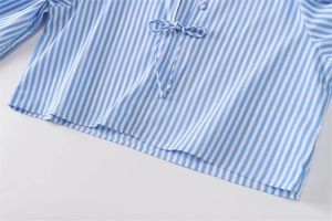 Dettaglio di camicia in popeline a righe bianche e blu con fiocco al collo e trama fine