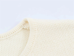 Detail of soft cream knit texture showing the neckline and shoulder seam craftsmanship